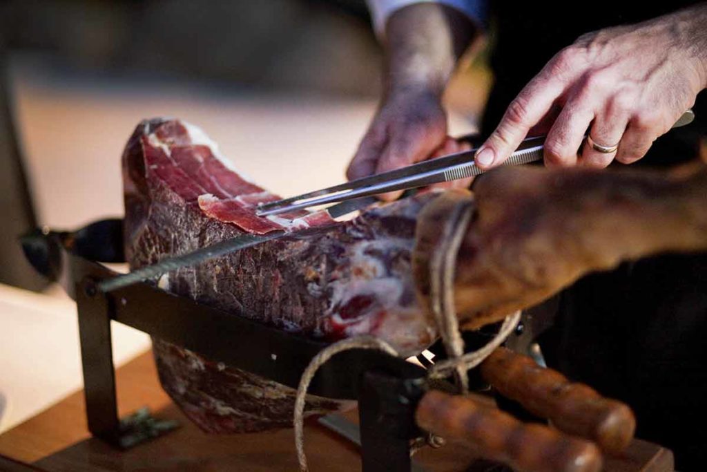 Homme découpant un jambon cru